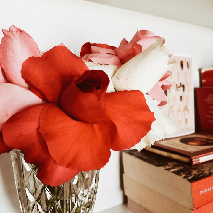 A bunch of pink, white and red roses sitting in a vase on a bookshelf. 