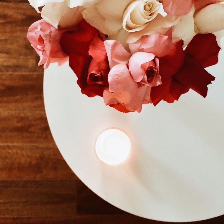 A bunch of roses sitting on a white table beside a lighted candle. 