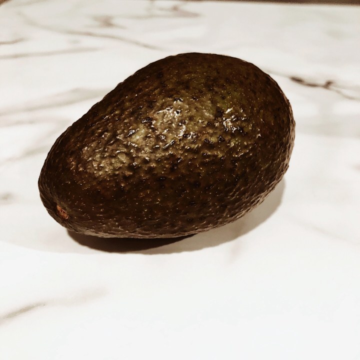 Hass avocado sitting on a black and white marbled surface.