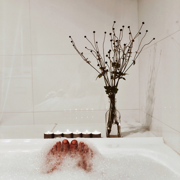 Feet in a bubble bath with candles and a bunch of flowers.