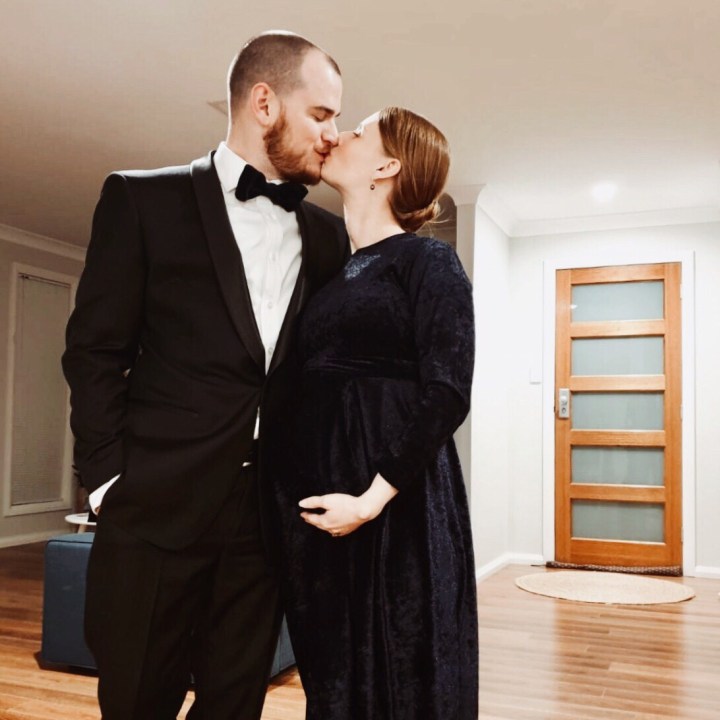 Couple in black tie outfits, kissing in a lounge room.