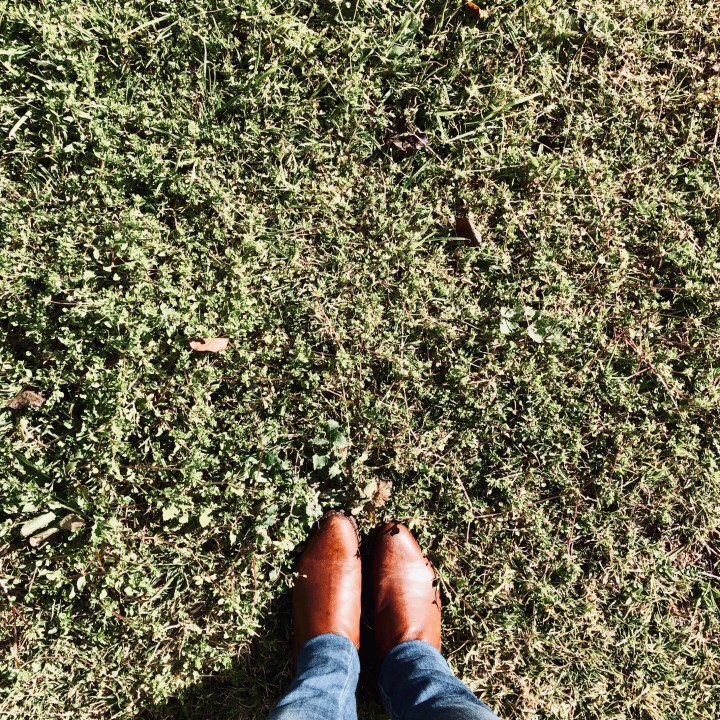 Woman in tan boots standing on green grass.