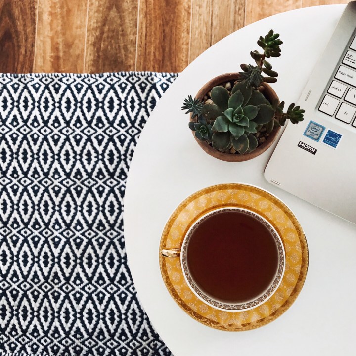 Looking down on a cup of tea, succulent and laptop sitting on a white table.