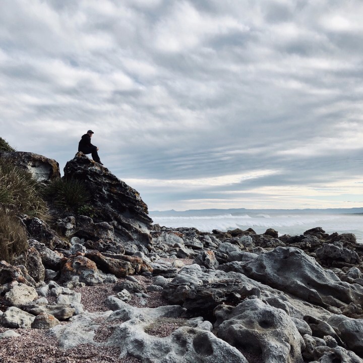 Man sitting on a rock at Bherwerre Beach in Booderee National Park, Australia.
