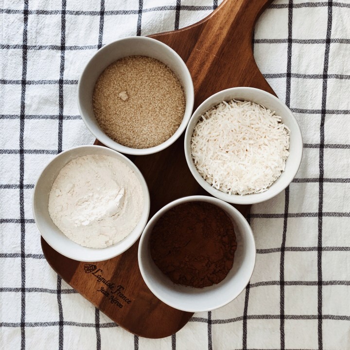 Dry ingredients for chocolate slice in ramekins on a wooden board.. 