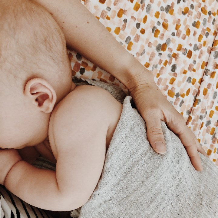Baby snuggled into mother on bed.