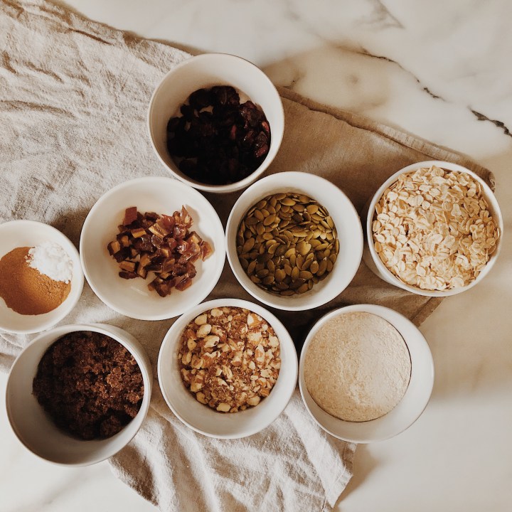Ingredients for granola biscuits in ramekins atop of a linen tea towel on a marble look benchtop.