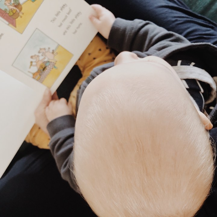 Looking down on a baby boy sitting in his mother's lap, reading a book.