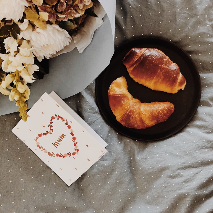 Bunch of flowers, Mother's Day card and pastries sitting on a bed.