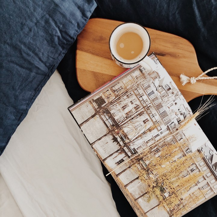Cup of coffee and open book sitting on a navy blue linen duvet