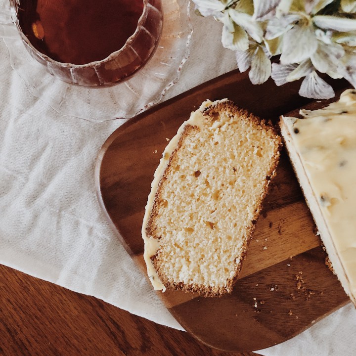 A slice of Madeira cake, alongside a cup of tea and bunch of dried hydrangeas.