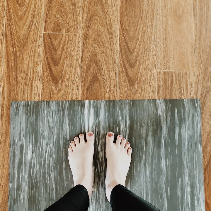 Looking down on feet standing on a grey and white yoga mat.