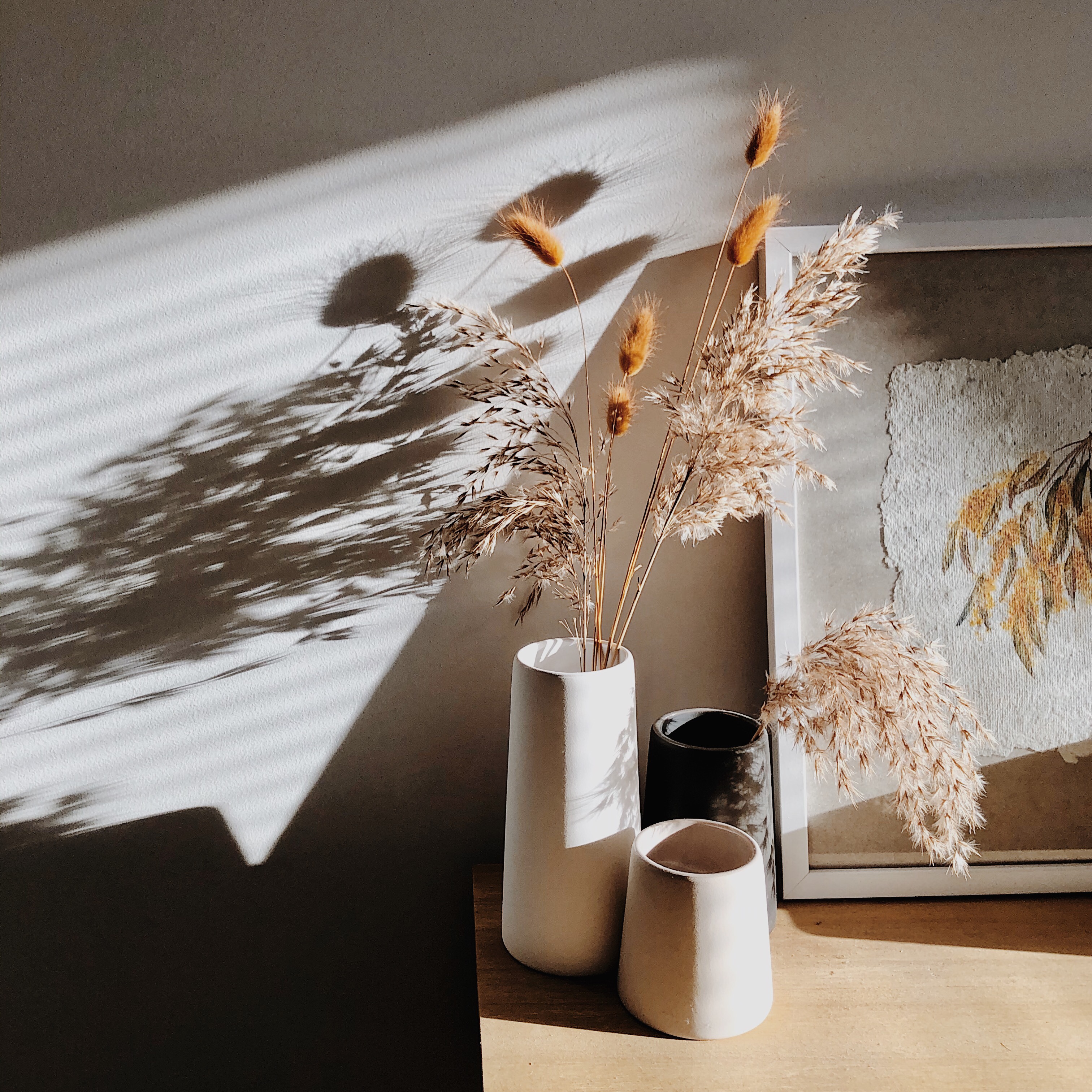 Dried grasses in vases sitting on a console table in the late afternoon light.