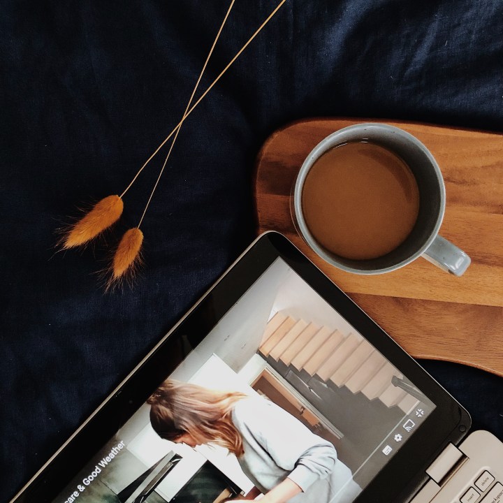 Looking down at a laptop and cup of coffee sitting on a navy blue linen duvet.