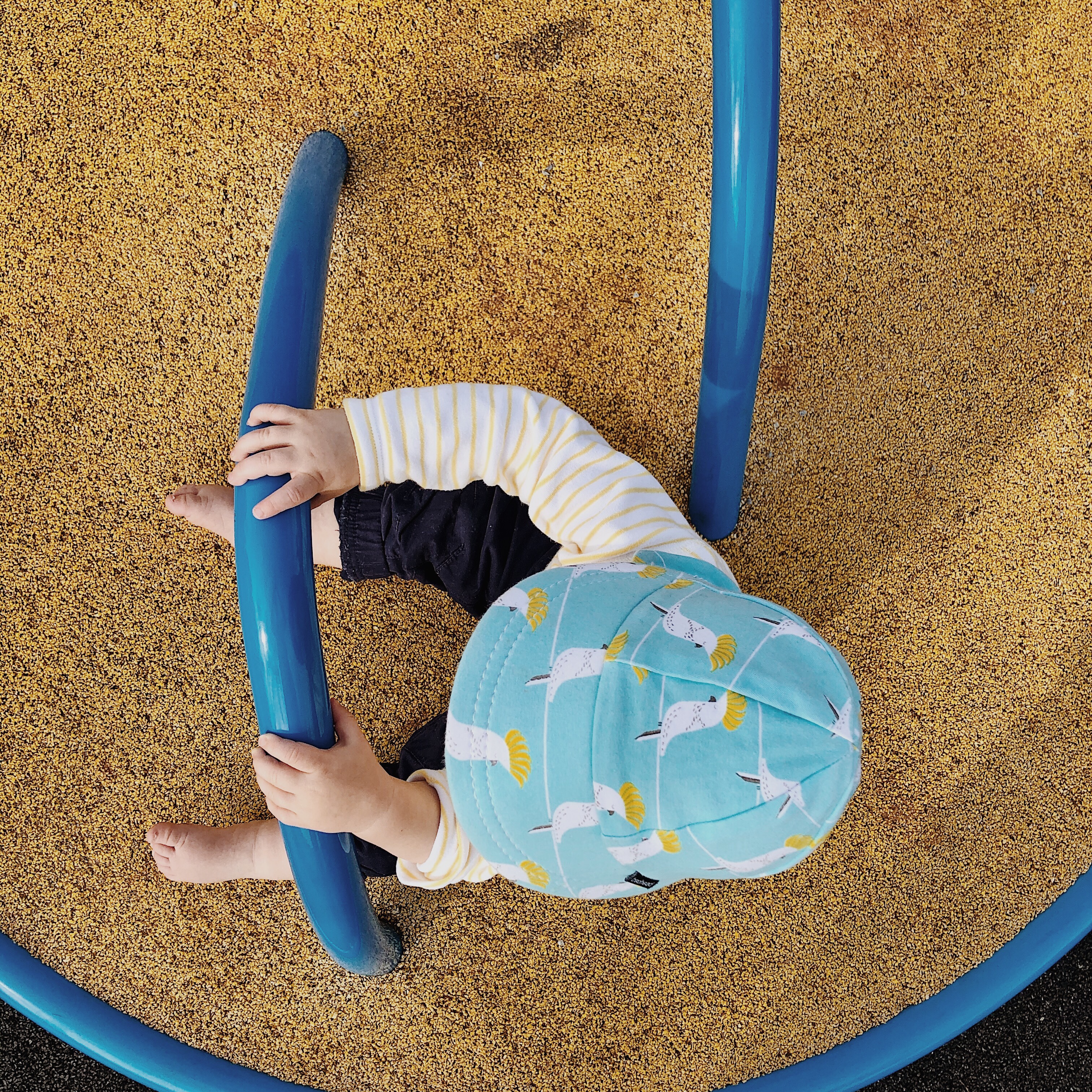 Looking down at a baby boy sitting on a merry-go-round at park.