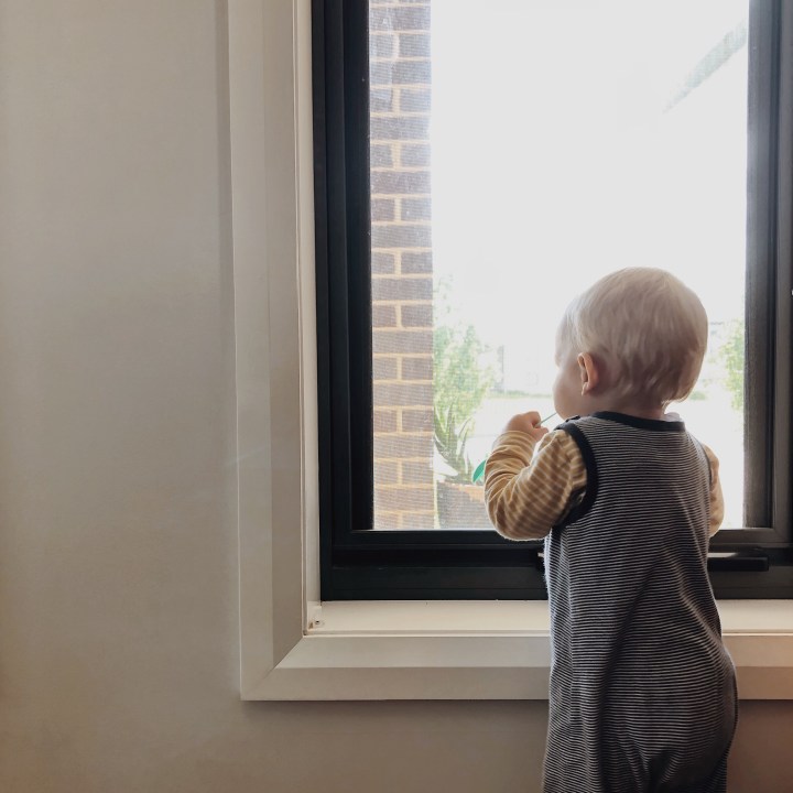 Infant boy staring outside through a window.