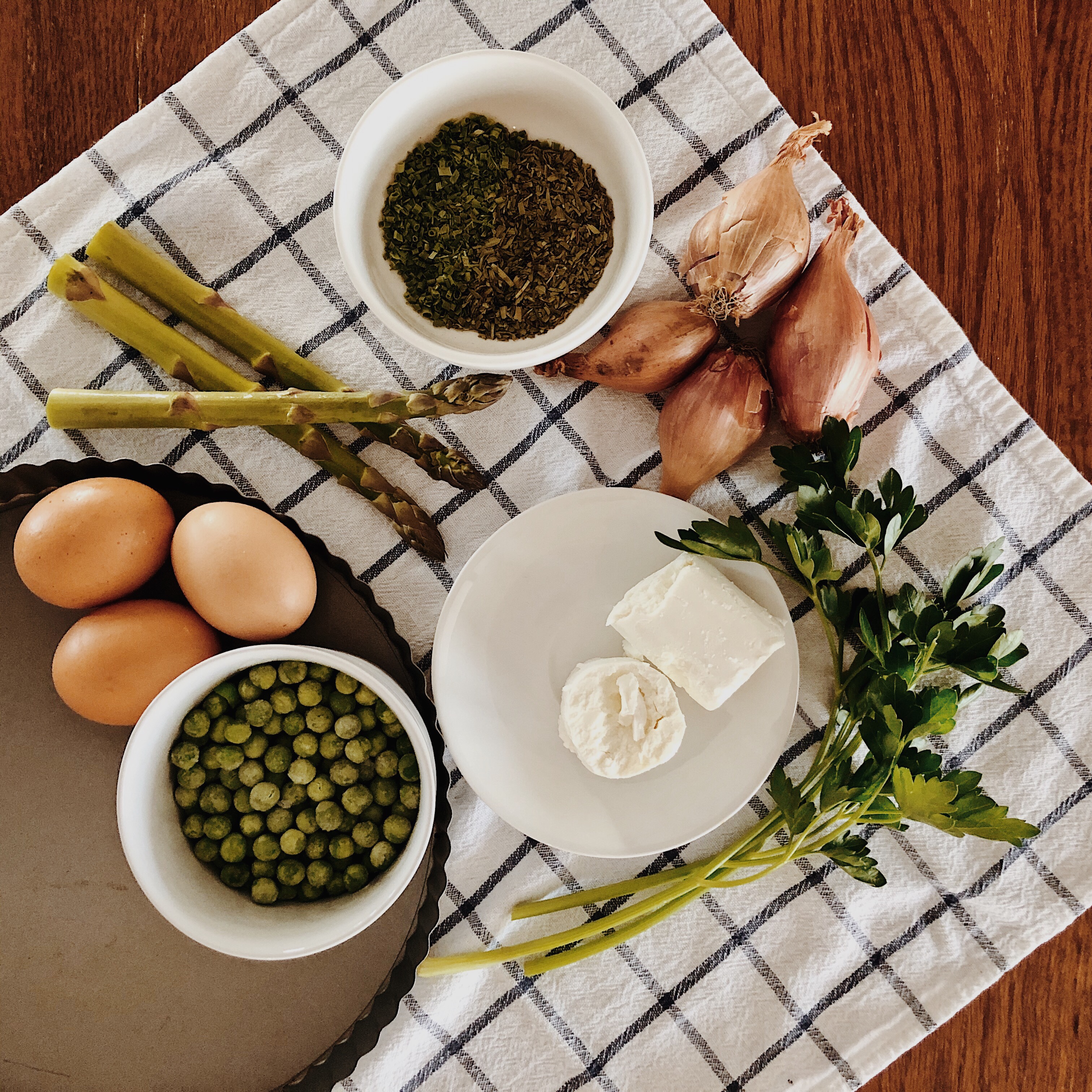 Ingredients for spring vegetable and goat's cheese tart on a blue and white check tea towel.