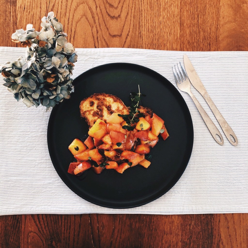 French toast with caramelised peaches and thyme on a blue and white stripe placement beside a sprig of dried hydrangeas.
