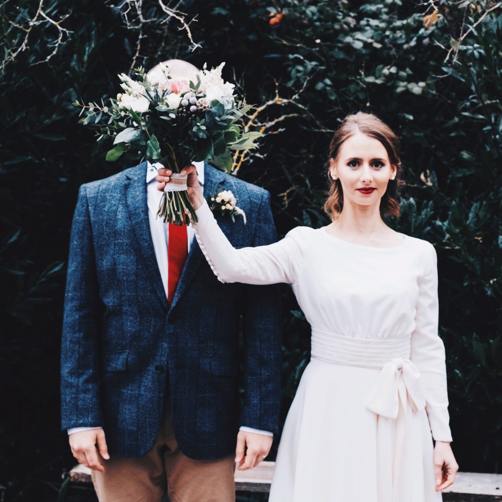 Bride holding her wedding bouquet over the groom's face.