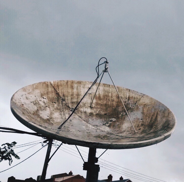 Looking up at a weathered satellite dish set amongst a grey sky.