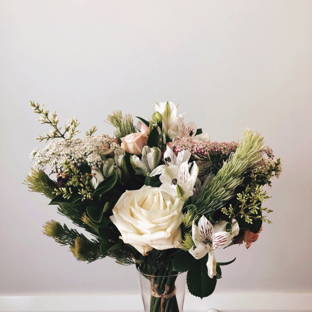 Bunch of white, pink and green flowers set against a light grey wall.