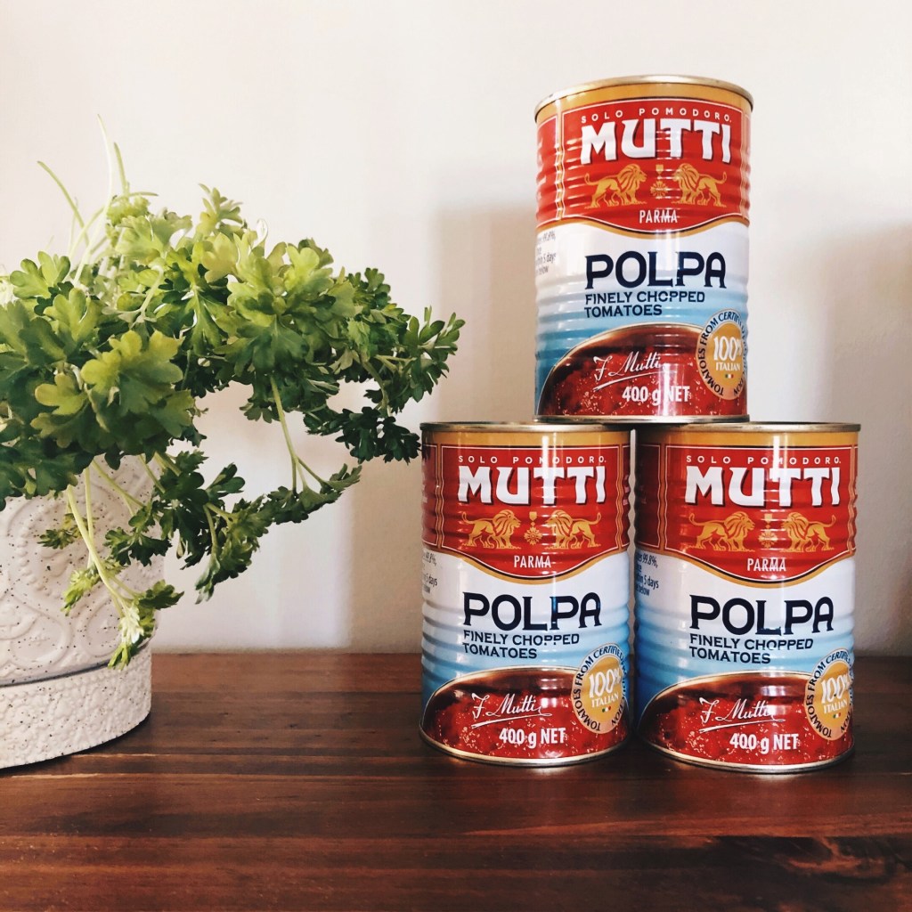 Cans of Mutti Polpa tin tomatoes beside a pot of parsley.