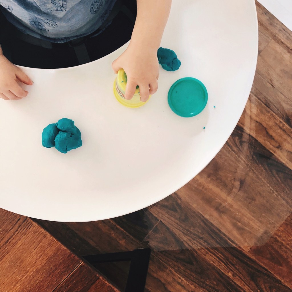 Toddler playing with Play Doh in a highchair.