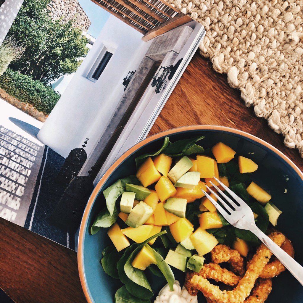 Calamari, spinach, mango and avocado salad beside an open magazine.