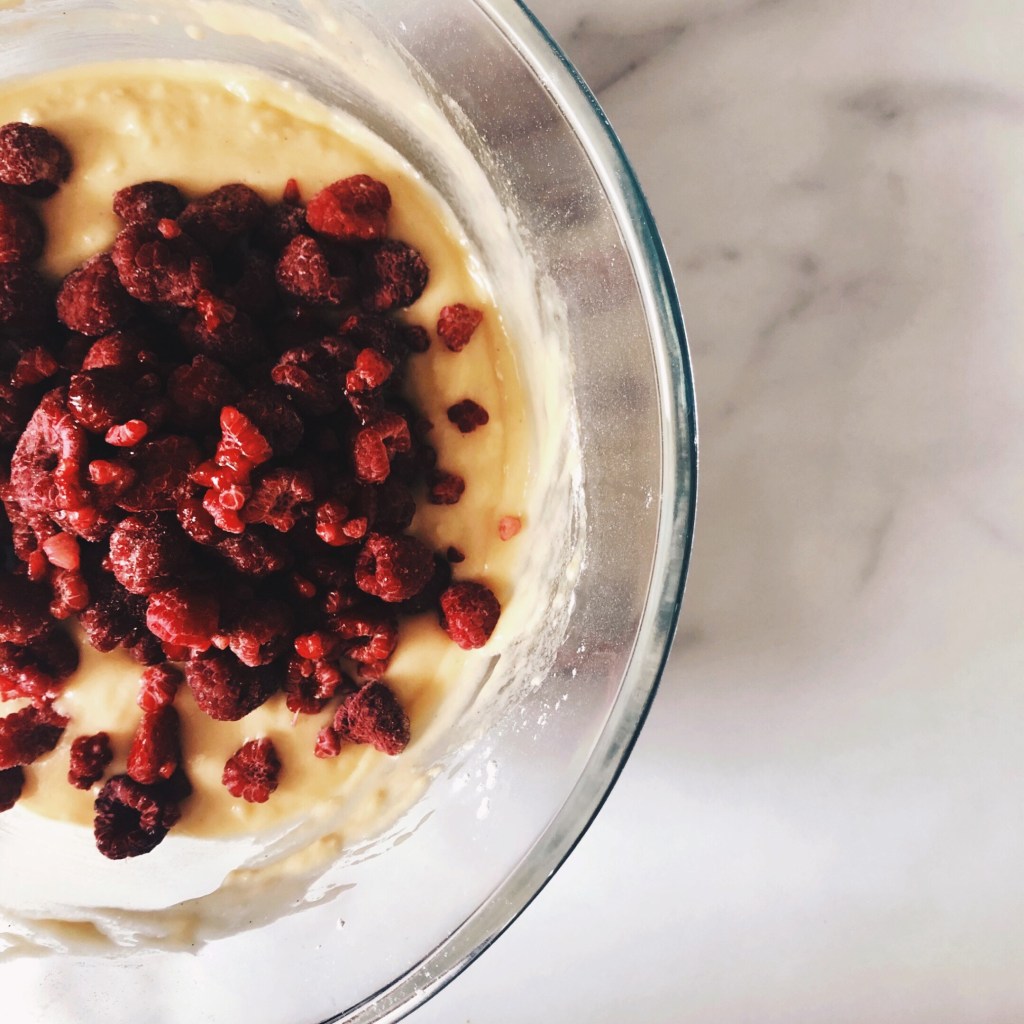 Frozen raspberries sitting atop of a basic muffin mixture in a glass bowl.