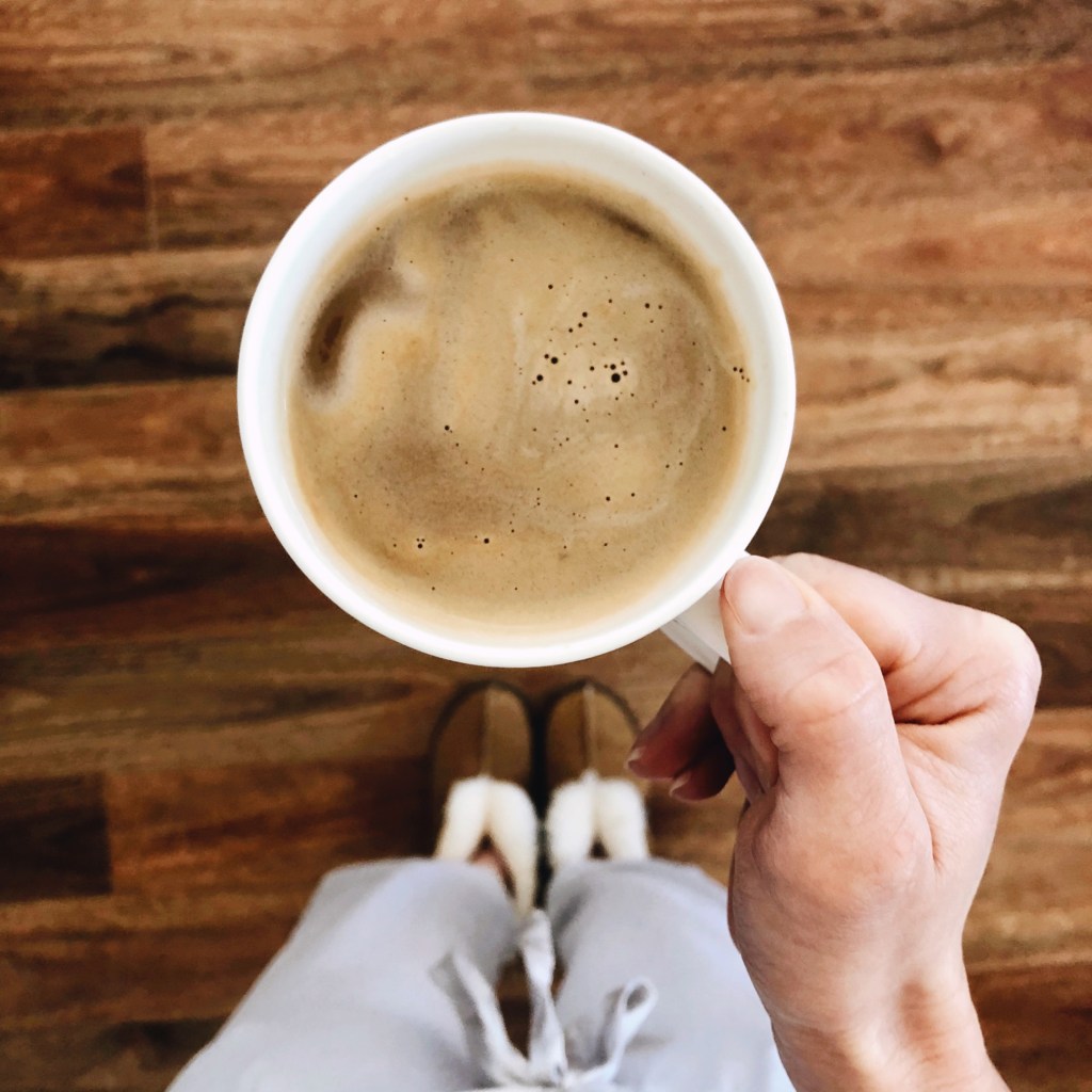 A woman in pyjamas looking down on a cup of coffee. 