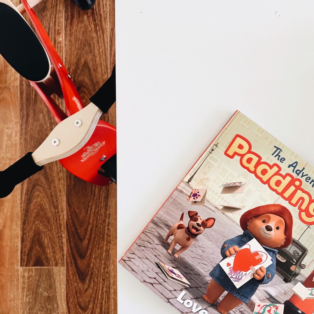 Looking down on a red child's trike and a Paddington Bear book.