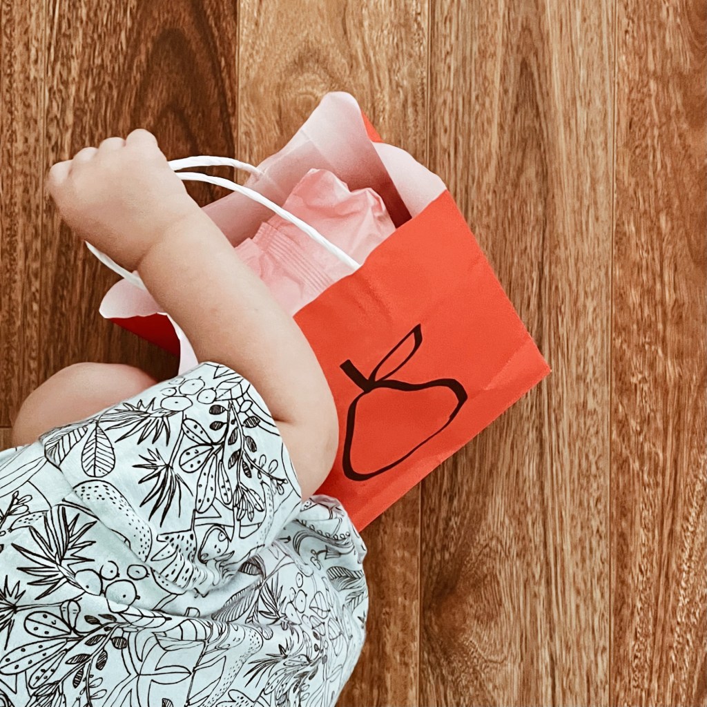 Toddler clasping a small paper shopping bag.