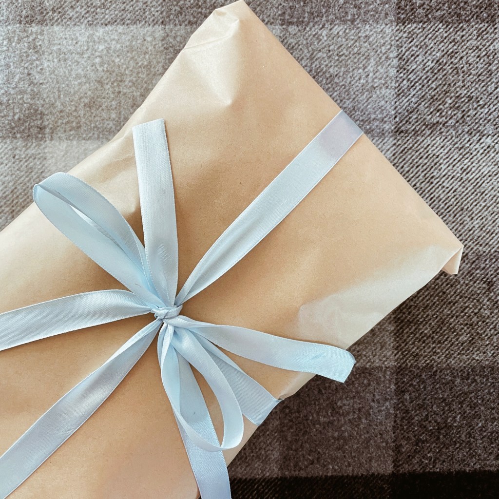 Looking down on a gift wrapped in brown paper and tied with a light blue ribbon, set against a black and white checked blanket.