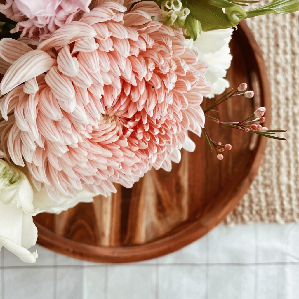 Looking down on a pink striped dahlia in an arrangement sitting on a wooden tray on a jute table table runner.