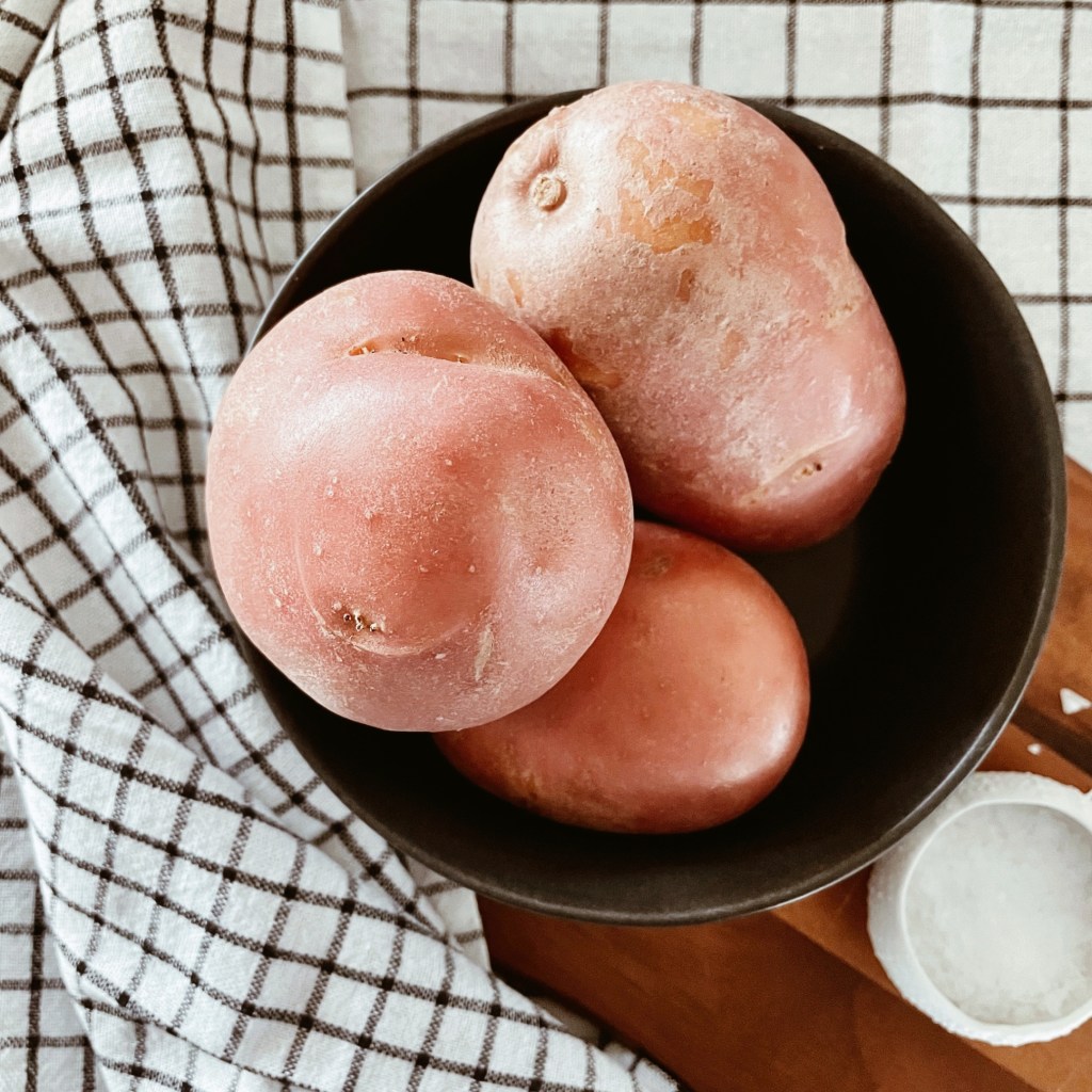 Red potatoes in a bowl on a wooden board besides a salt dish, surrounded by checked cotton tea towels.