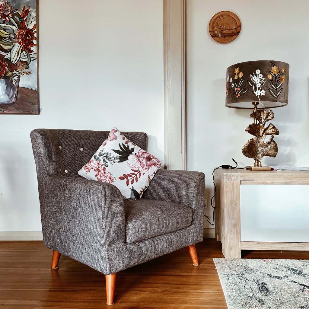 Grey armchair beside a long tv-unit with decorative lamp.