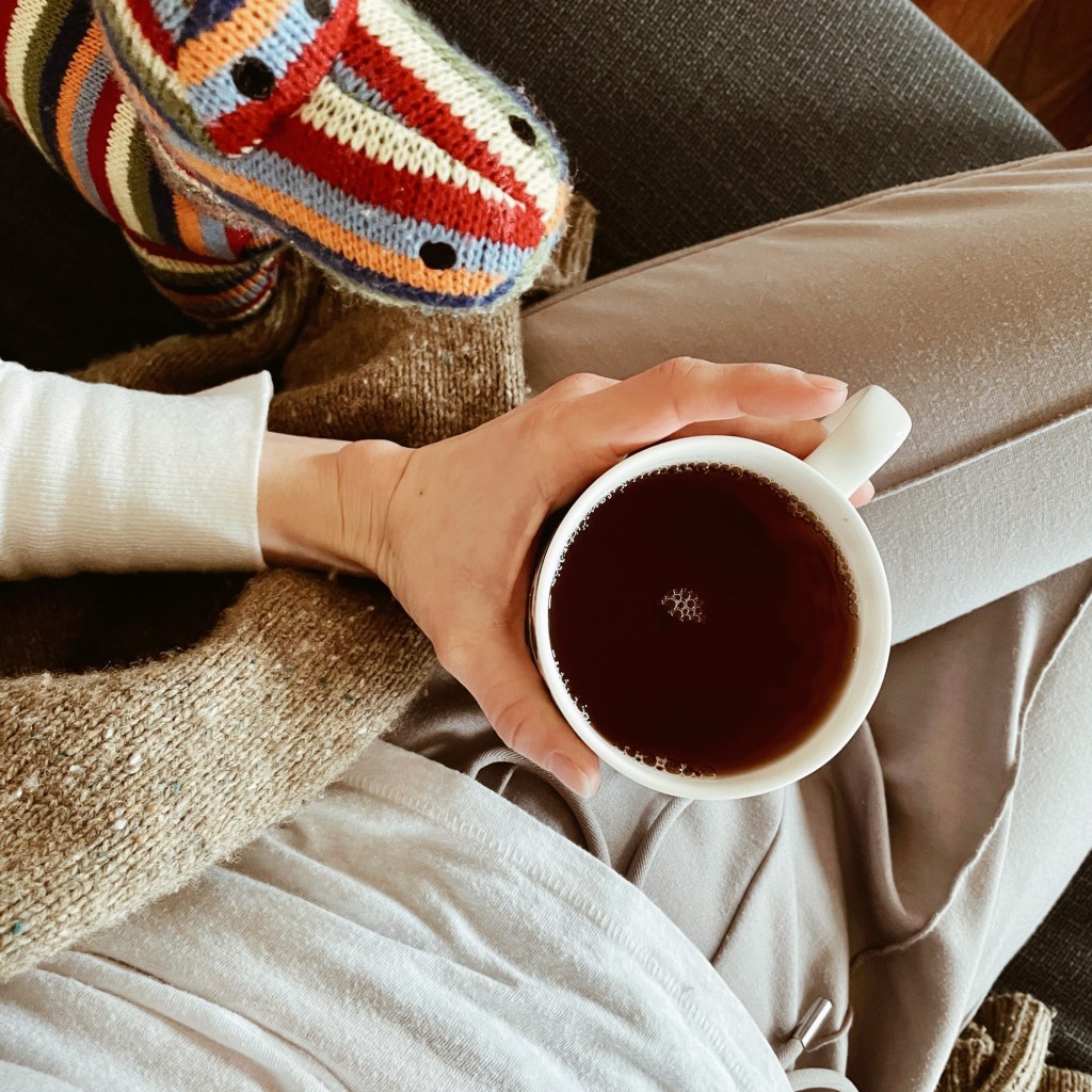 Woman holding cup of tea beside a stuffed dinosaur toy.