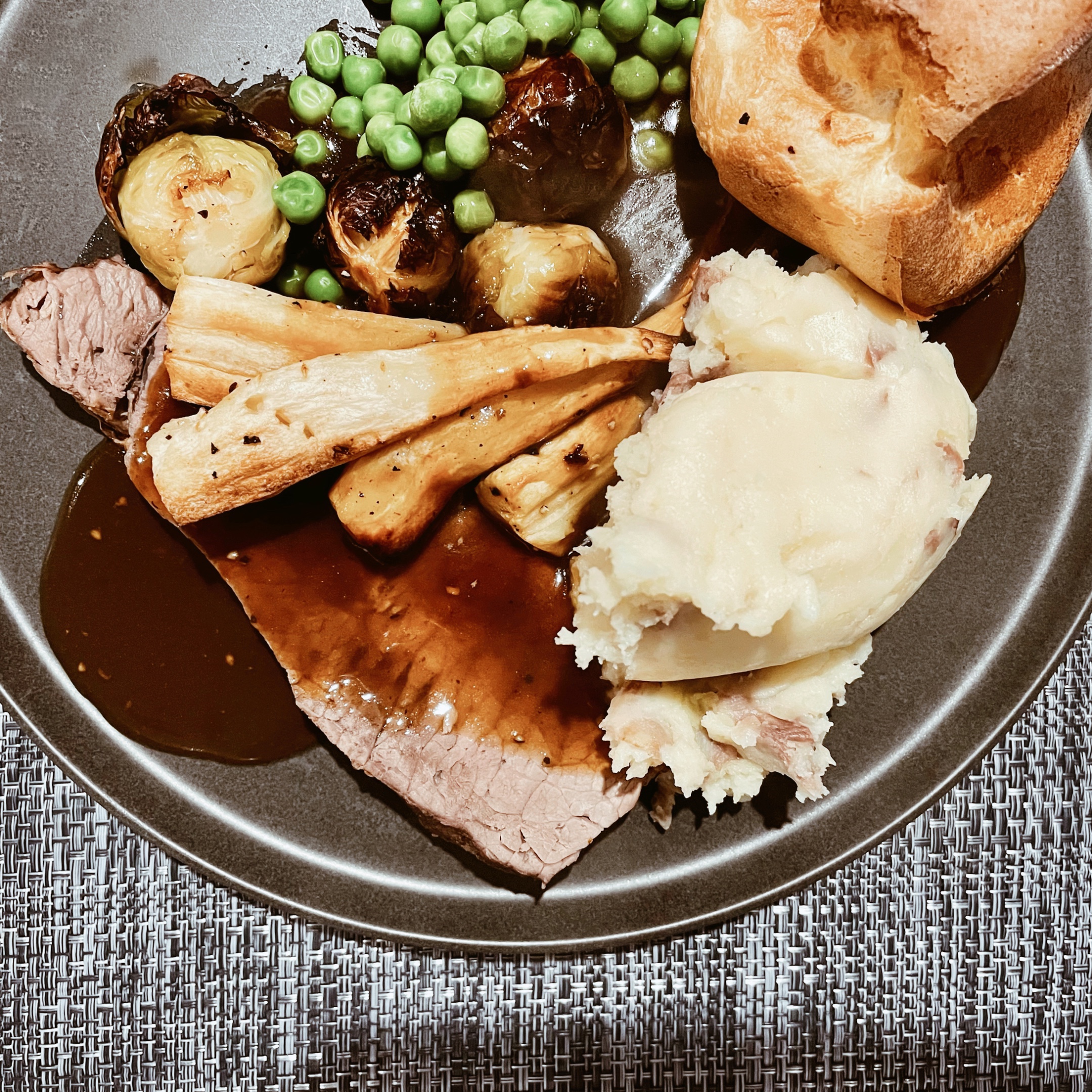 Looking down on a plate of roast beef, mashed potato, Yorkshire pudding, peas, Brussels sprouts and parsnips.