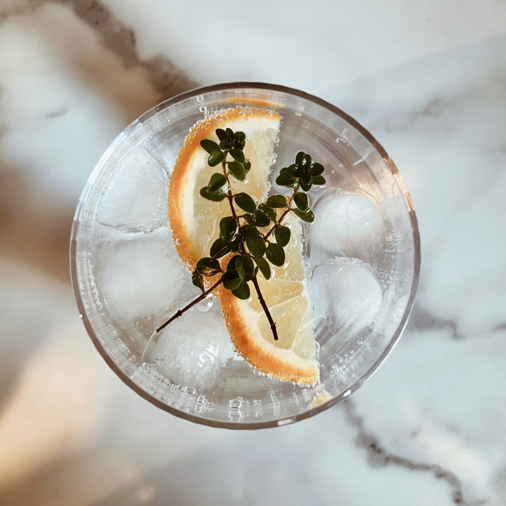 Looking down on a gin and tonic in a glass, garnished with lemon wedges and sprigs of thyme.