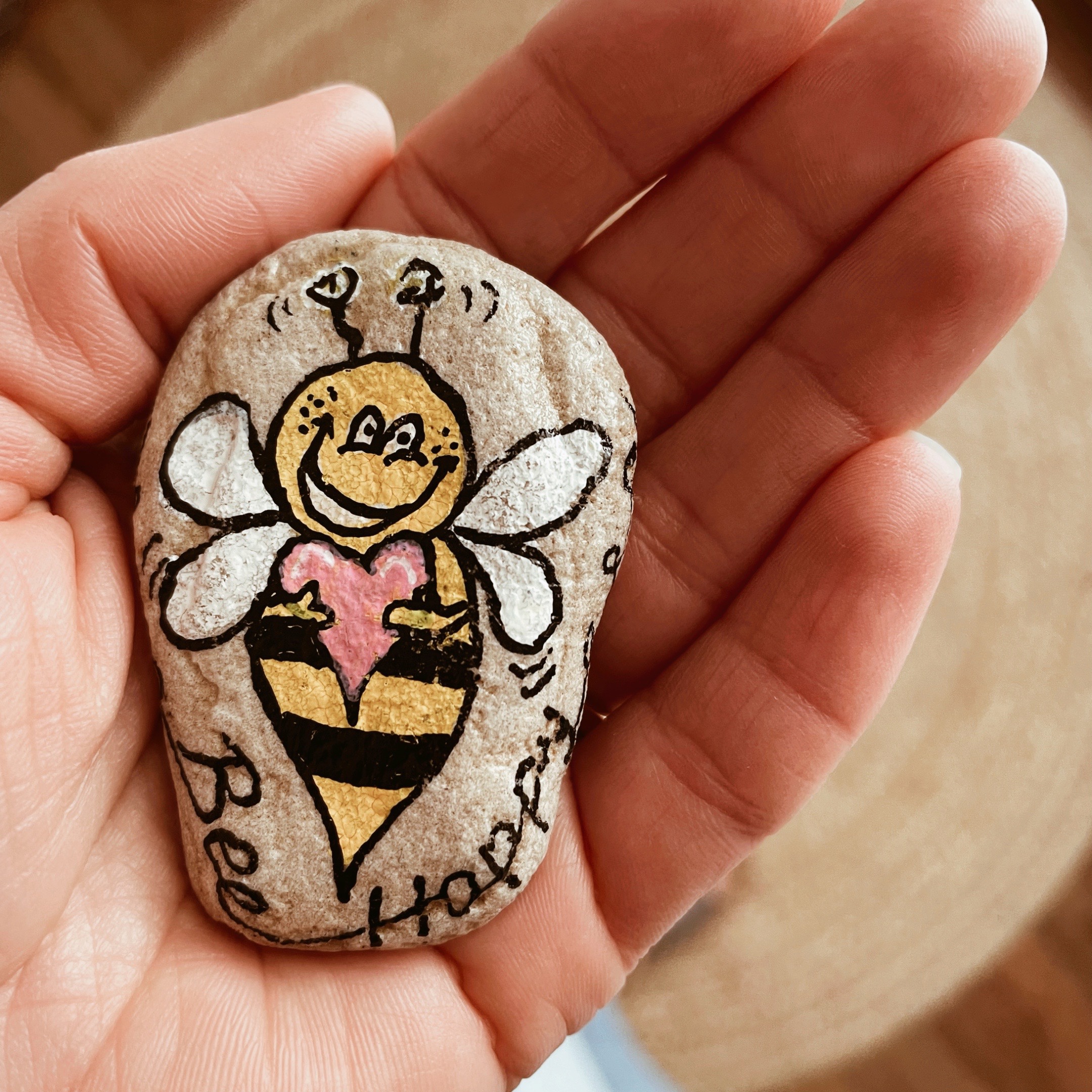 Hand holding a rock painted with 'Bee Happy'