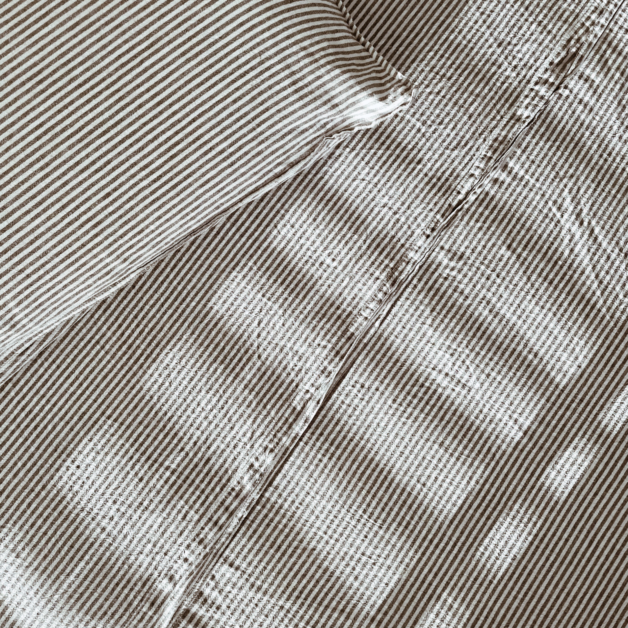 Looking down on a bed made up with grey and white striped linen sheets.