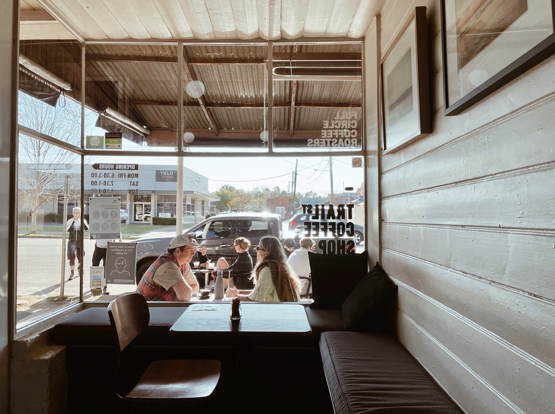 Looking through the front window of a coffee shop to people sitting at tables outside.