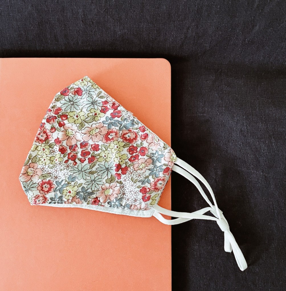 A floral mask sitting on a peachy pink notebook.