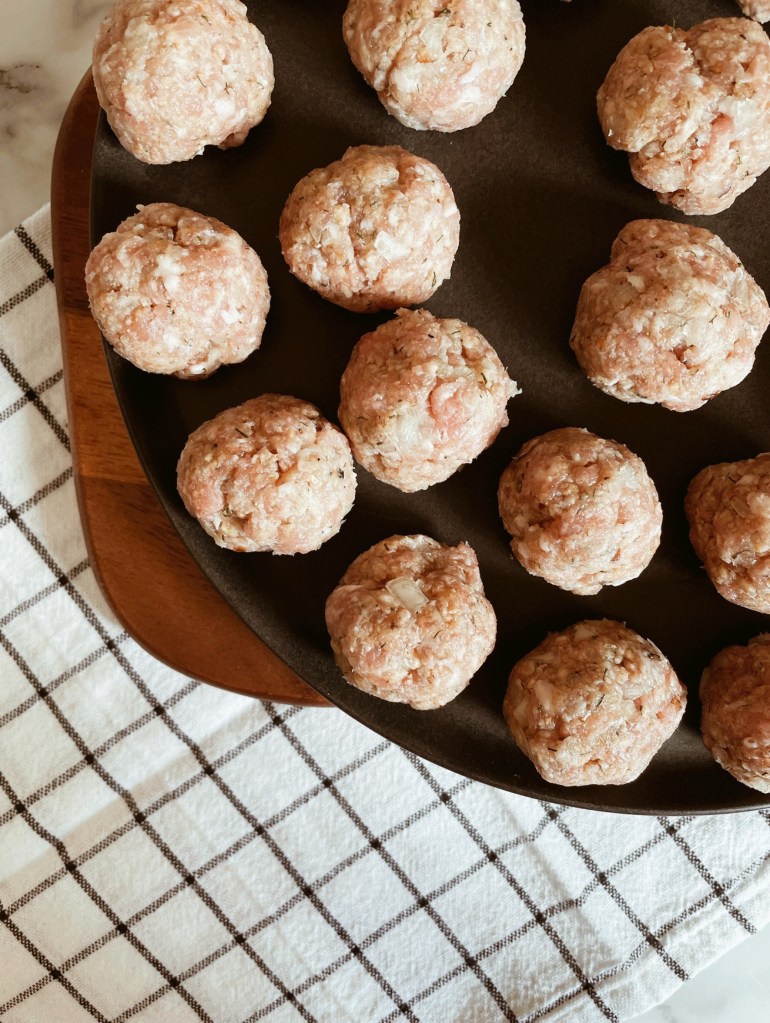 Raw meatballs on a plate, atop a black and white check teatowel.
