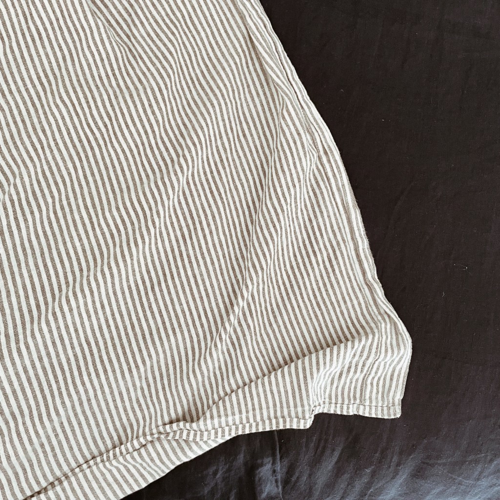 A striped sheet turned down over a linen navy blue duvet cover.