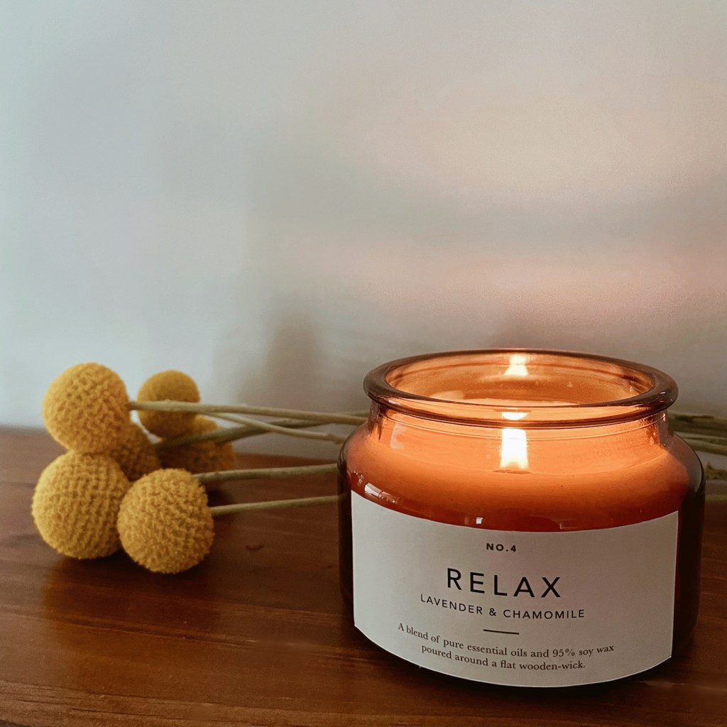 Lit candle in amber jar beside a bunch of billy button flowers.
