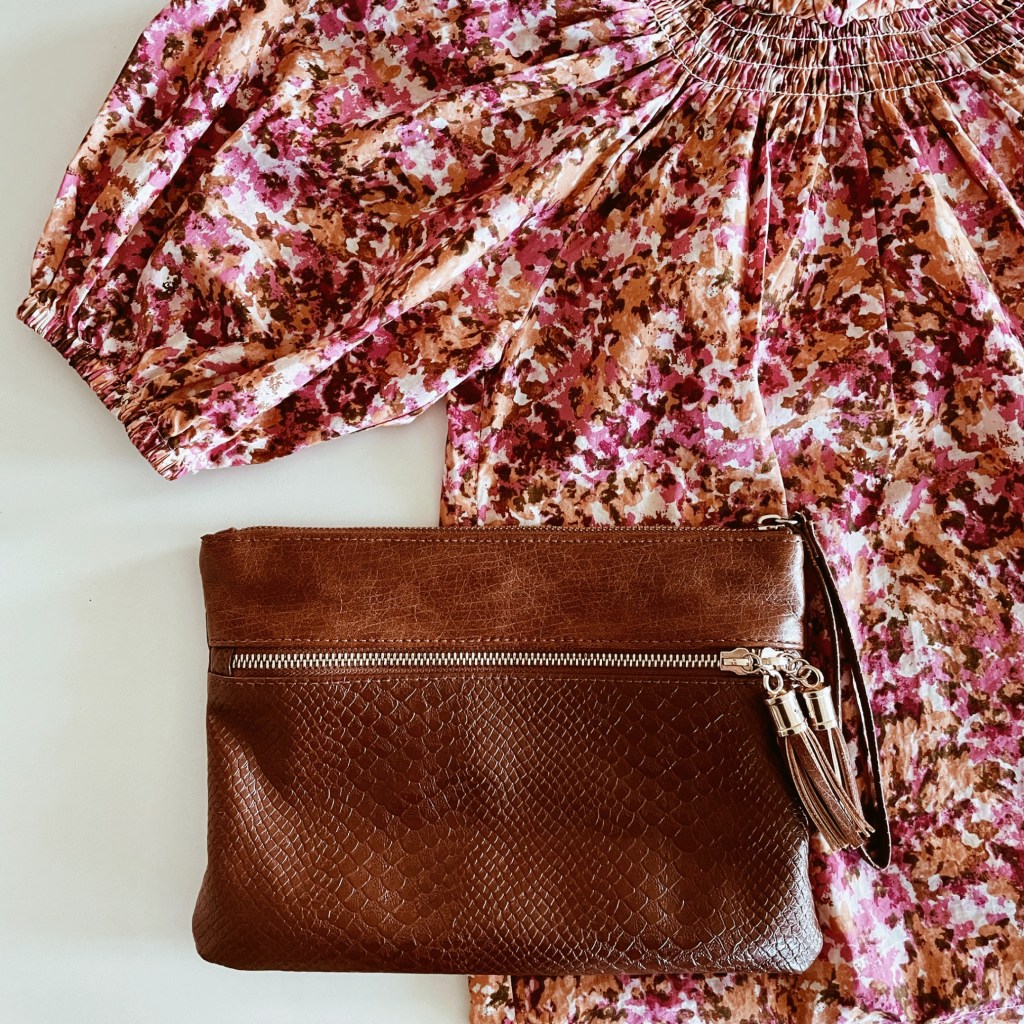 Pink, orange and brown blouse beside tan brown clutch bag.
