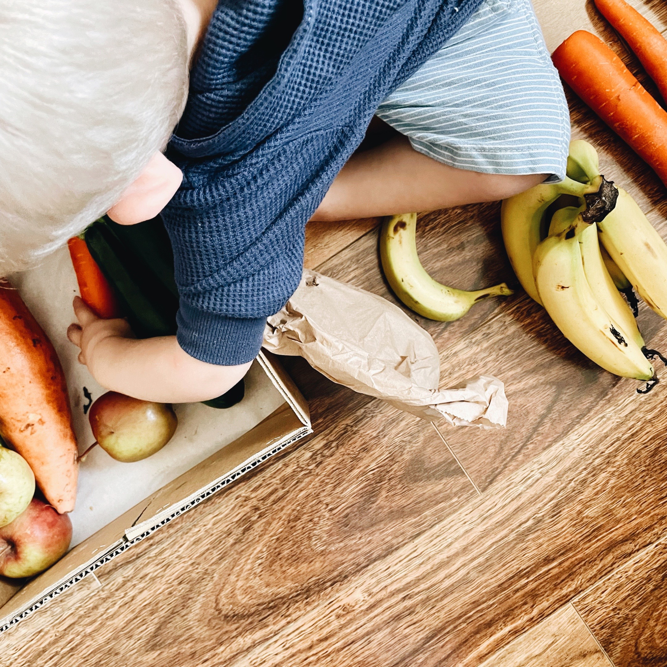 Looking down on a toddler boy helping to unpack a box of fruit and vegetables.