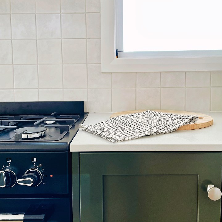 A black free-standing cooker beside an olive green kitchen cabinet with white benches.