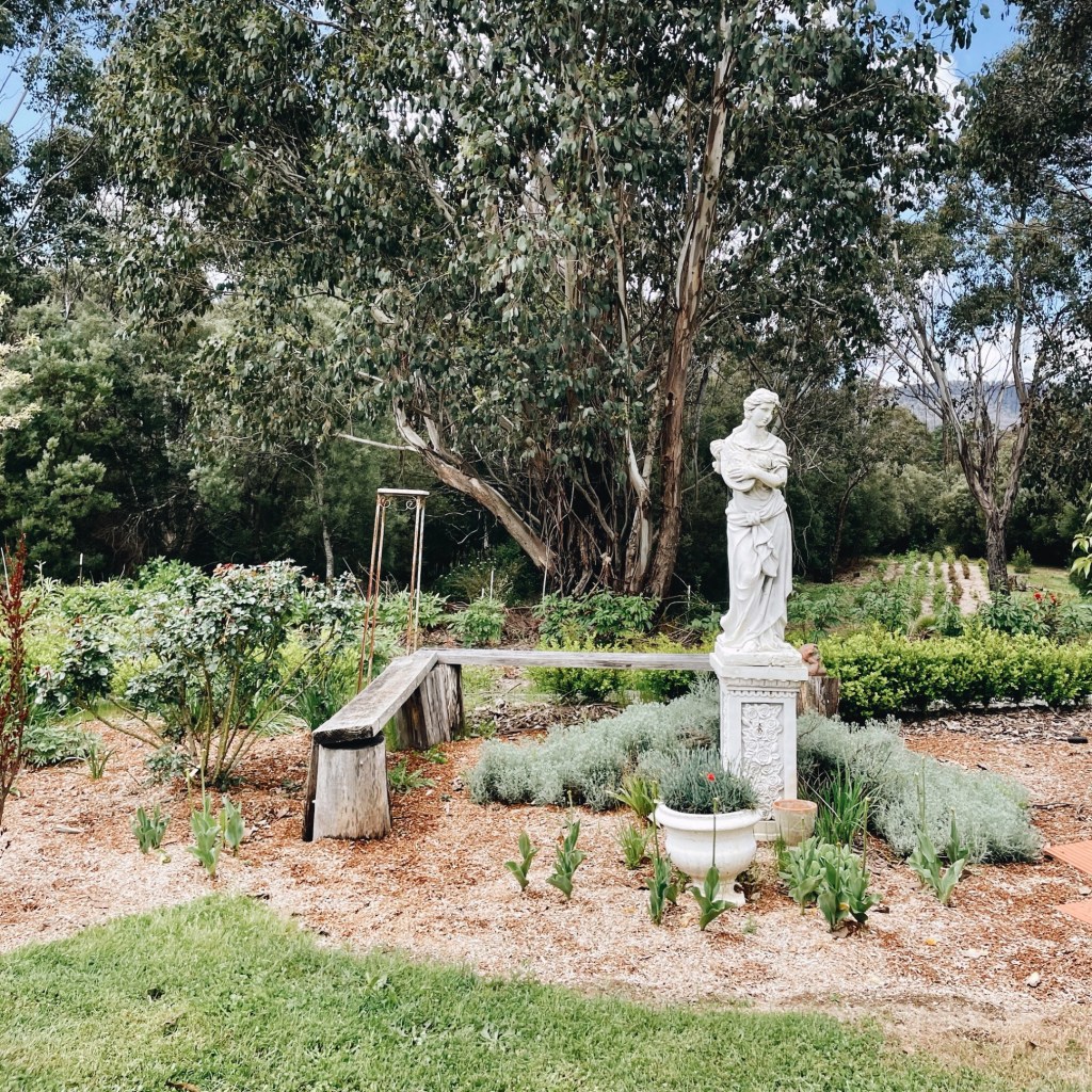 A statue stands in a garden bed, in front of bushland in Batlow, New South Wales, Australia.